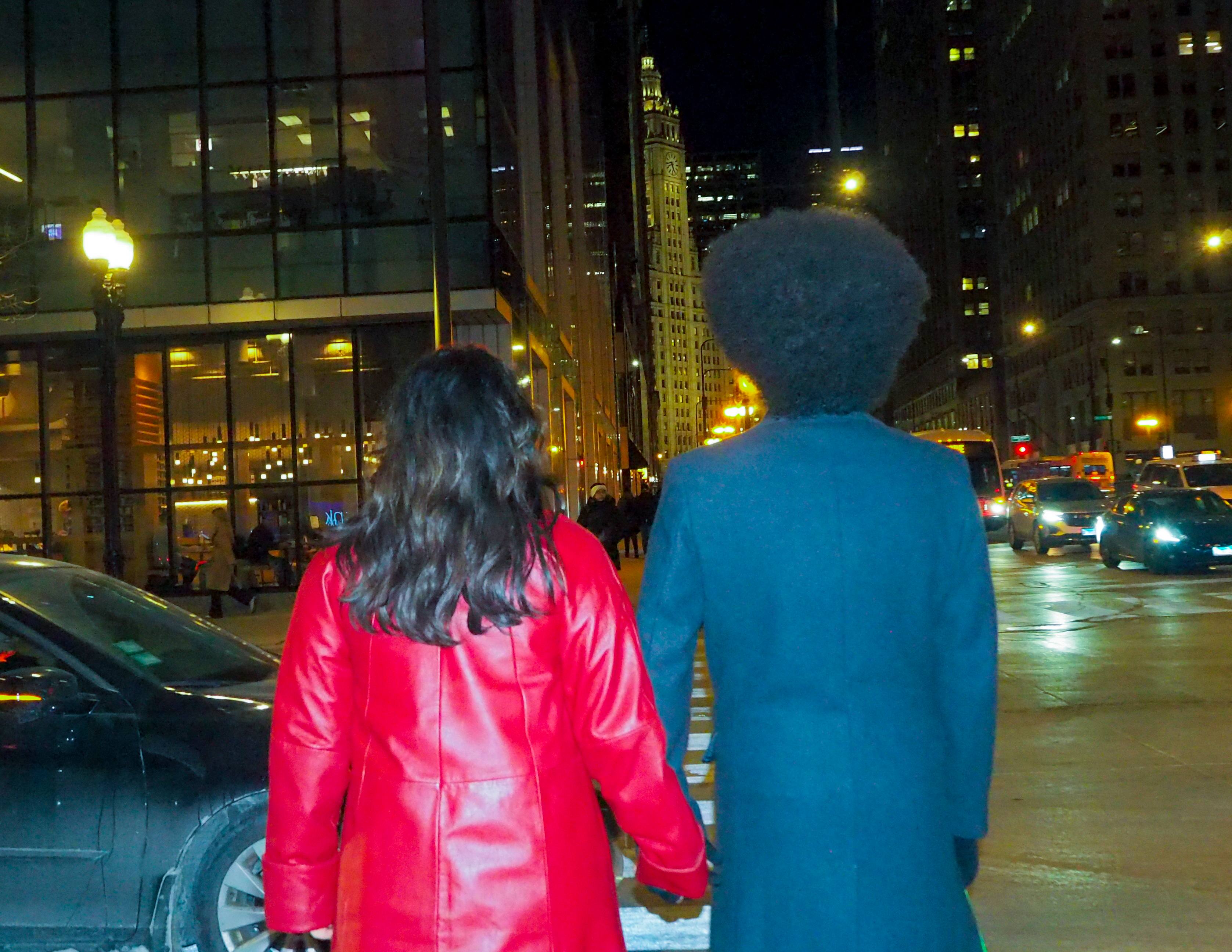 Couple holding hands on Chicago street at night with Wrigley Building in background